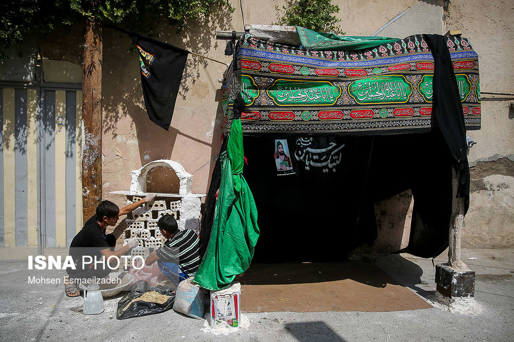 دو نوجوان در حال آماده سازی موکبی برای پذیرایی از  عزاداران در محله قلعه‌ ساختمان مشهد هستند.