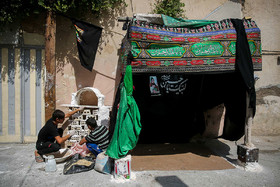 دو نوجوان در حال آماده سازی موکبی برای پذیرایی از  عزاداران در محله قلعه‌ ساختمان مشهد هستند.