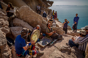 چند گردشگر نوازنده در حال نواختن ساز در دره مجسمه‌ها در جزیره هرمز هستند و مسافران در حال تماشا و تصویر برداری از آن‌ها هستند.