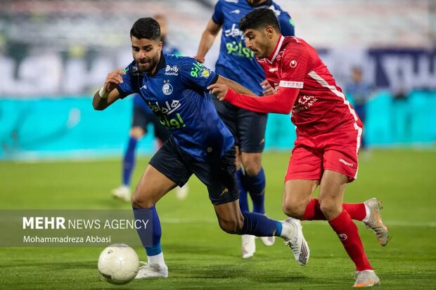 مهدی ترابی هافک تیم فوتبال پرسپولیس تهران در حال عبور توپ از محمد حسین مراد مند مدافع تیم فوتبال استقلال تهران است