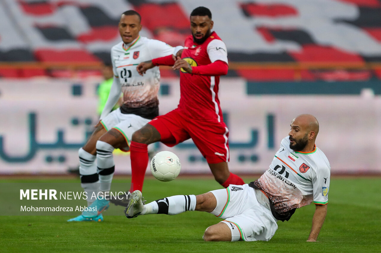 جورگن لوكاديا مهاجم تیم فوتبال پرسپولیس تهران در حال عبور توپ از رامتان سليمان زاده بازيكن تيم فوتبال مس رفسنجان در دیدار تیم های پرسپولیس تهران و مس رفسنجان است