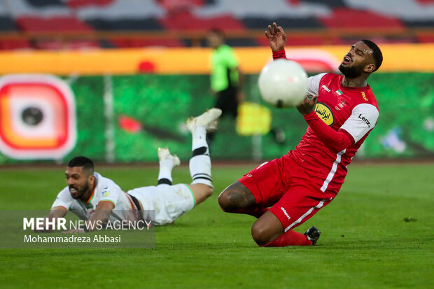 لحظه عبور توپ از مقابل جورگن لوكاديا مهاجم تیم فوتبال پرسپولیس تهران در دیدار تیم های پرسپولیس تهران و مس رفسنجان در تصویر دیده می شود